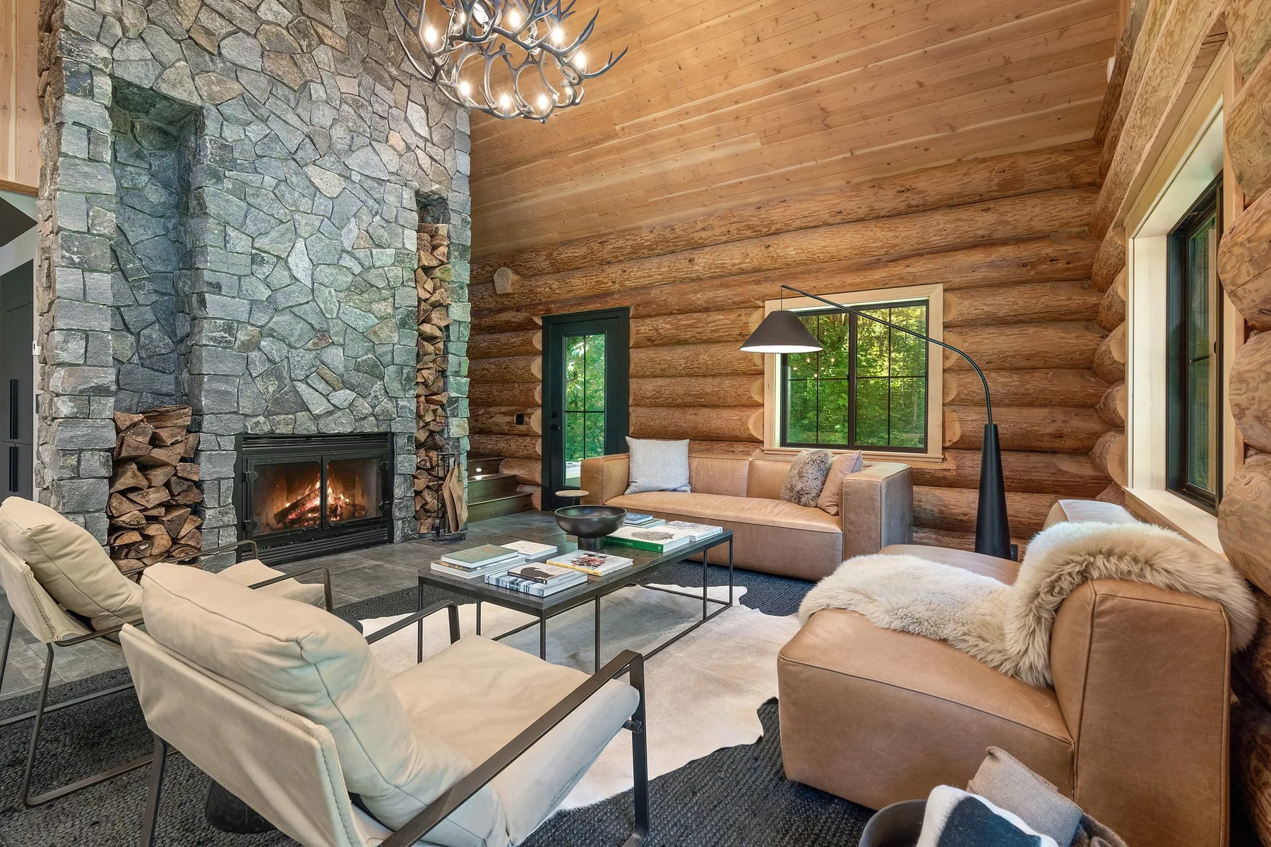 A spacious log-walled living room with seating arranged around a stone fireplace.
