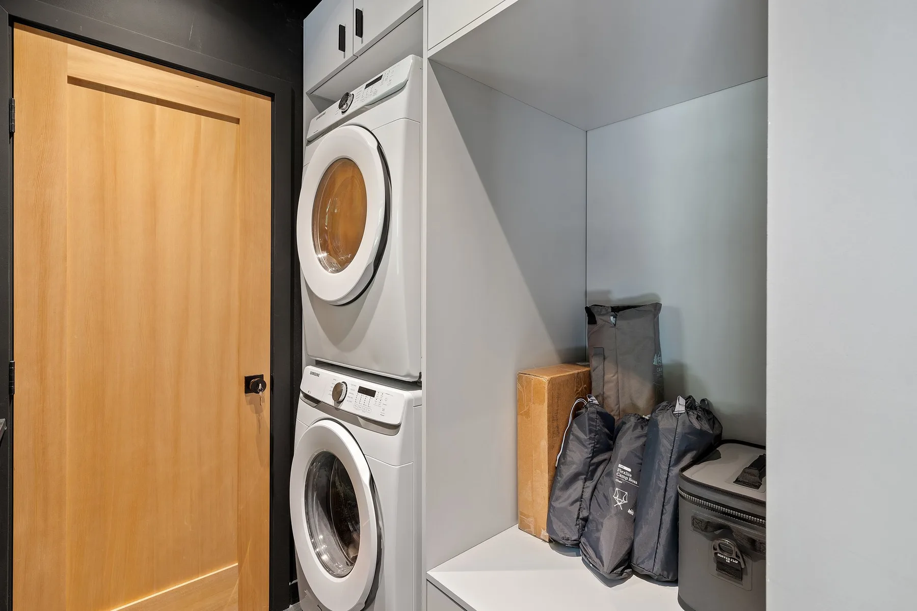 A laundry area with stacked front-loading machines and storage bags.