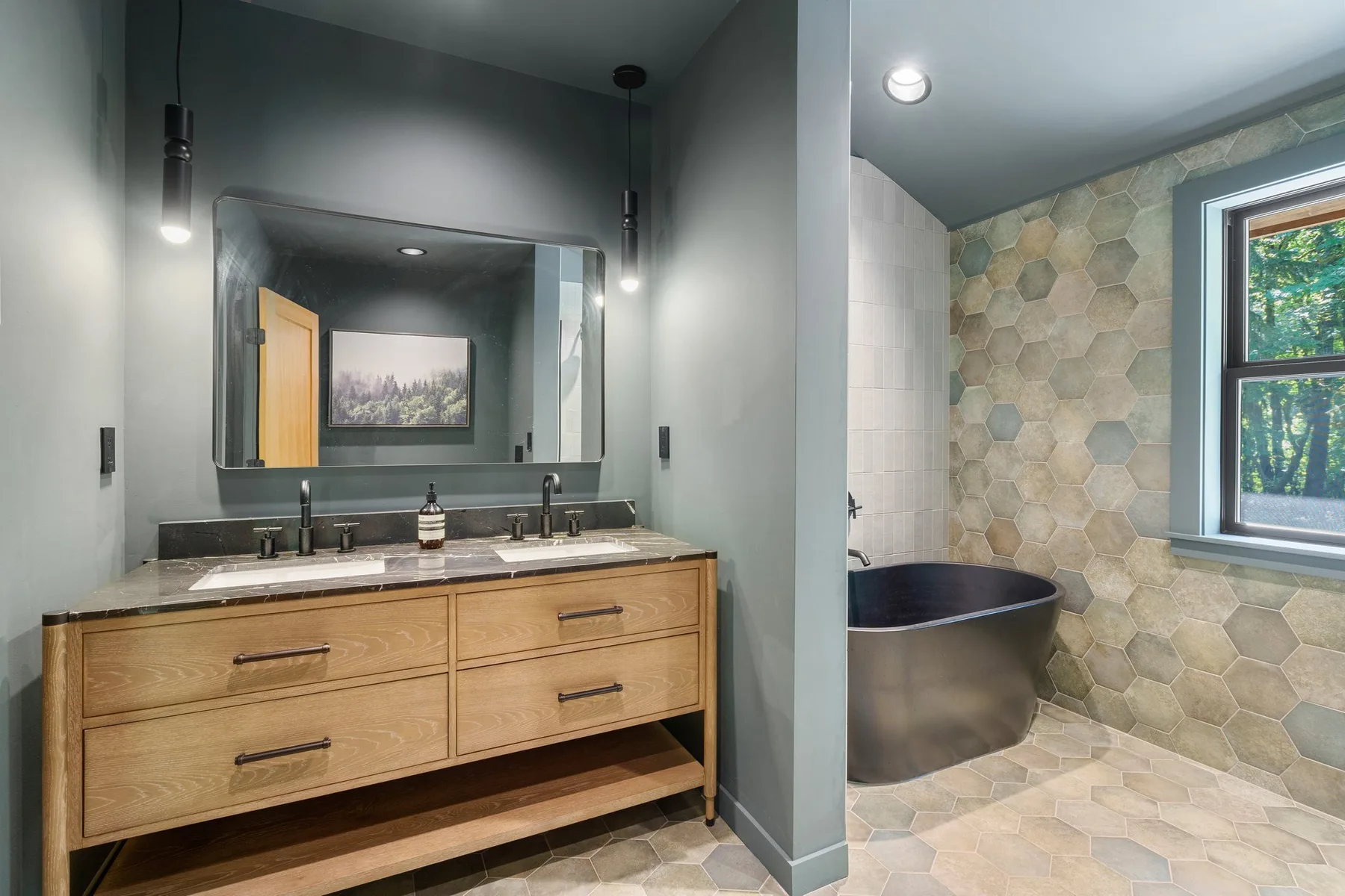 A bathroom with a wood vanity and a freestanding bathtub beside a window.