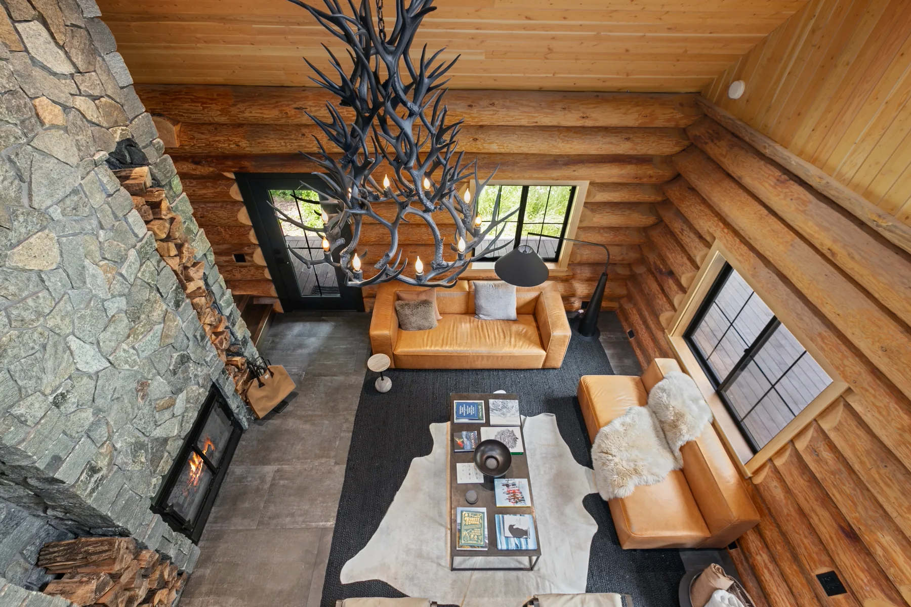 A log cabin living room with seating, a coffee table, and a stone fireplace.