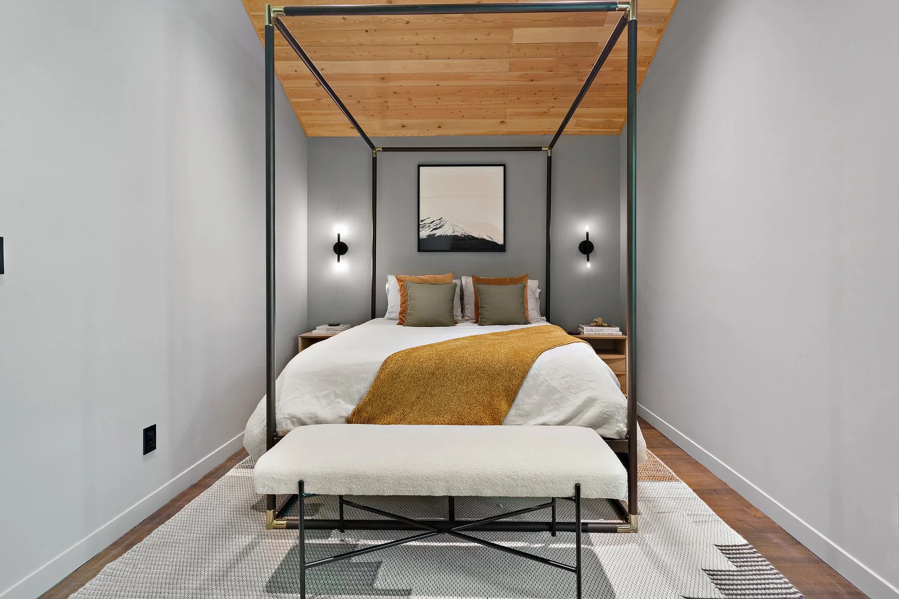 A bedroom with a bed beneath a wooden ceiling and a bench at its foot.