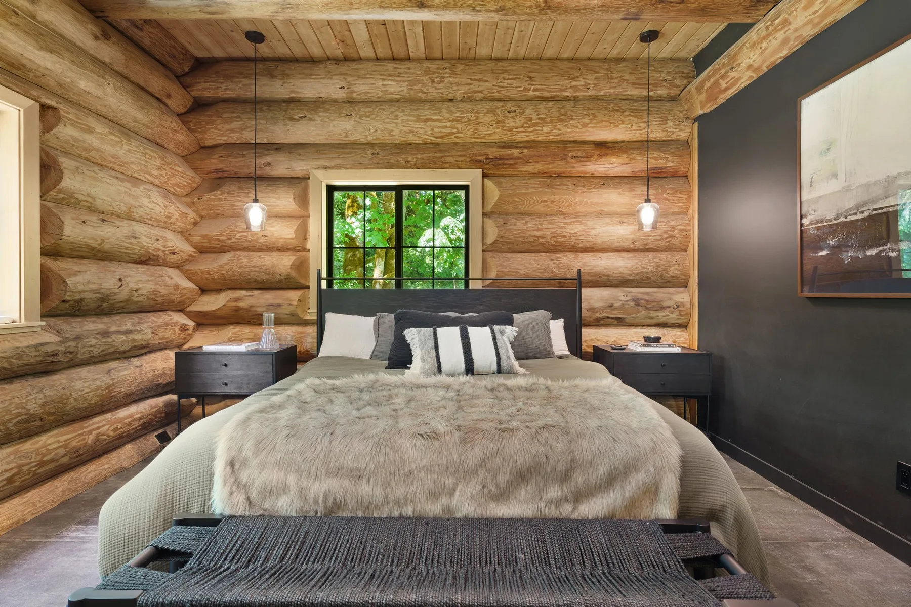 A bedroom with a bed beneath a window in a log-walled room.
