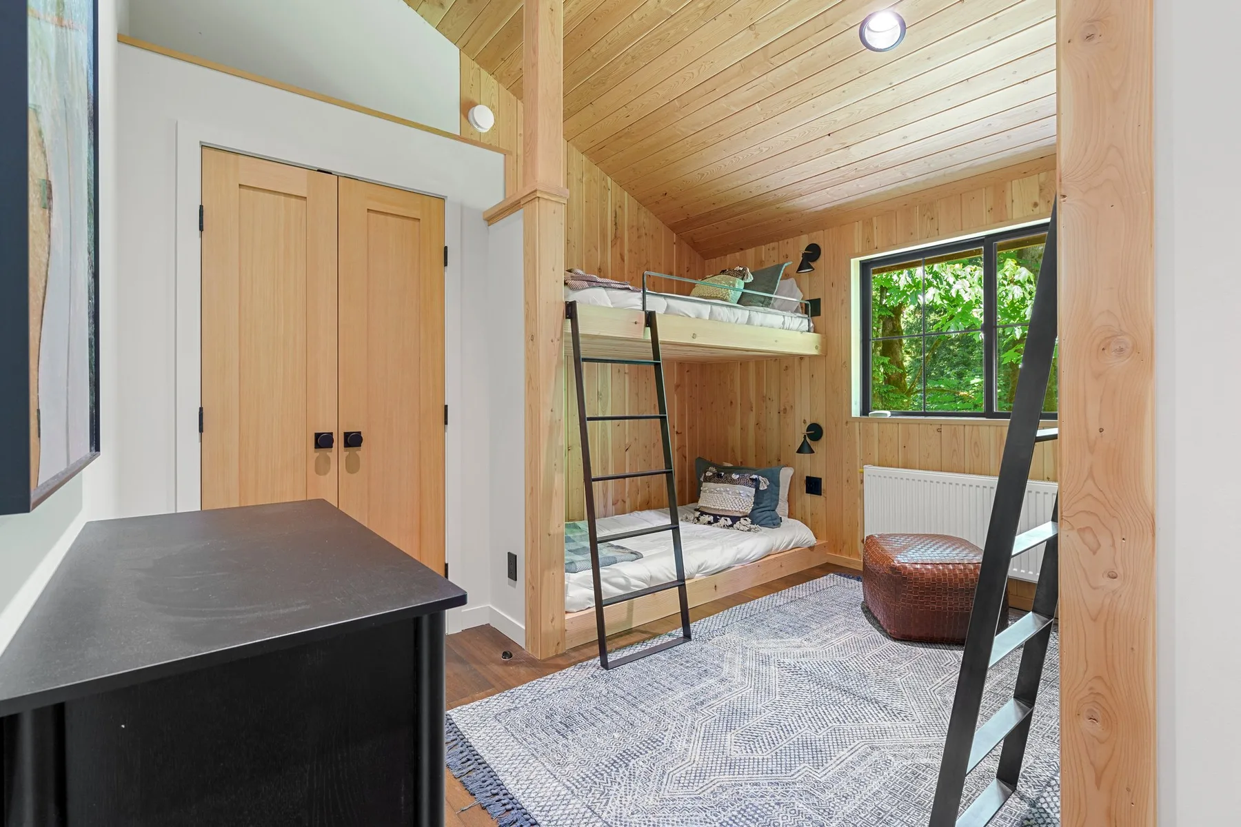 A wood-paneled bedroom with bunk beds, a desk, and a large window.