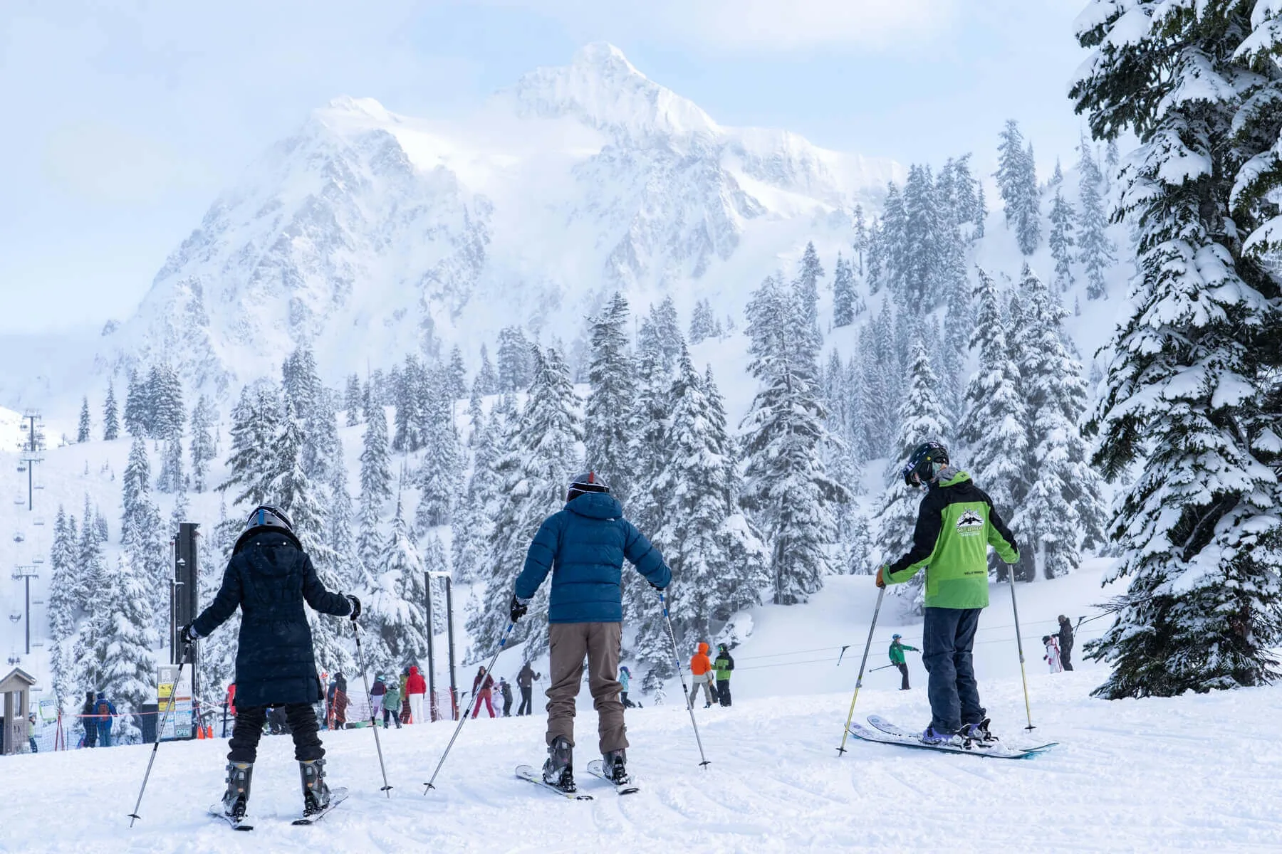 Skiers descend a snowy slope beneath a mountain backdrop.