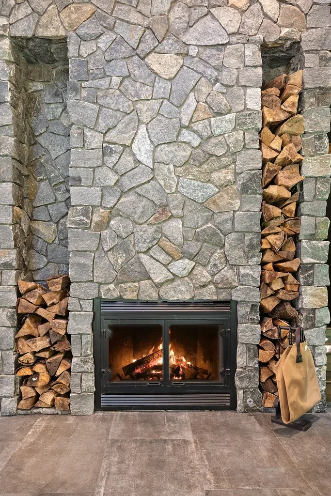 A stone fireplace with a glass-fronted fire and stacked firewood.
