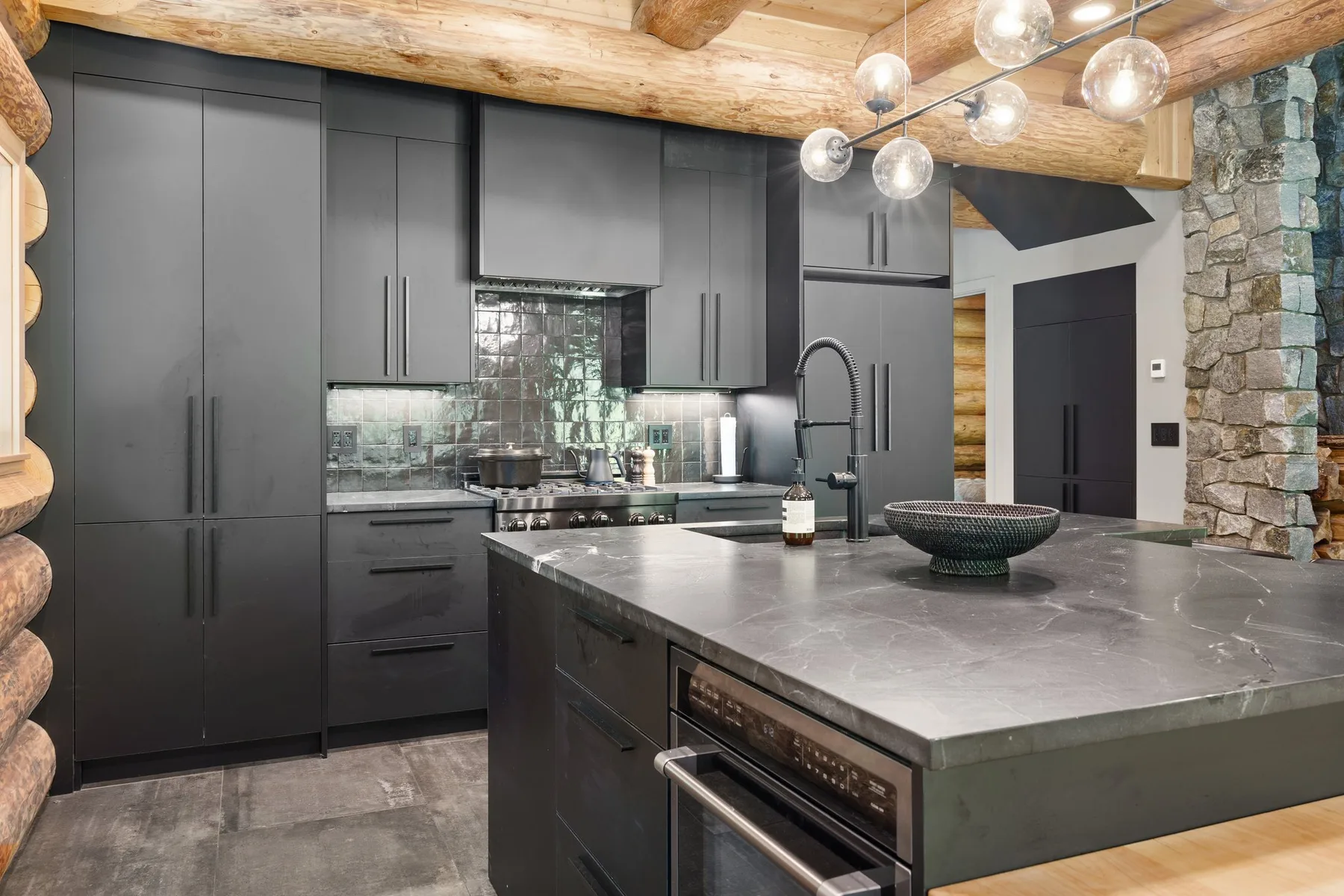 A modern kitchen with dark cabinetry, a large island, and exposed timber beams.