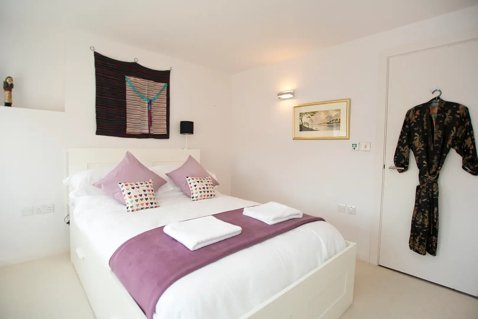 A bright bedroom with a neatly made bed and framed artwork on the wall.
