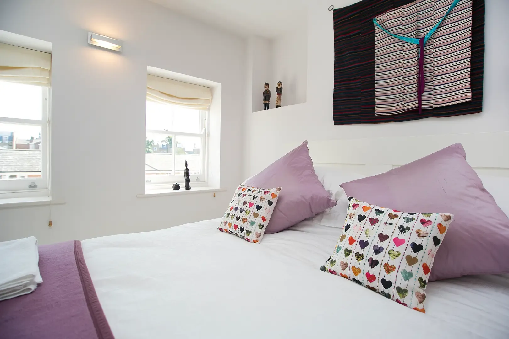 A bright bedroom with white bedding and colorful cushions.