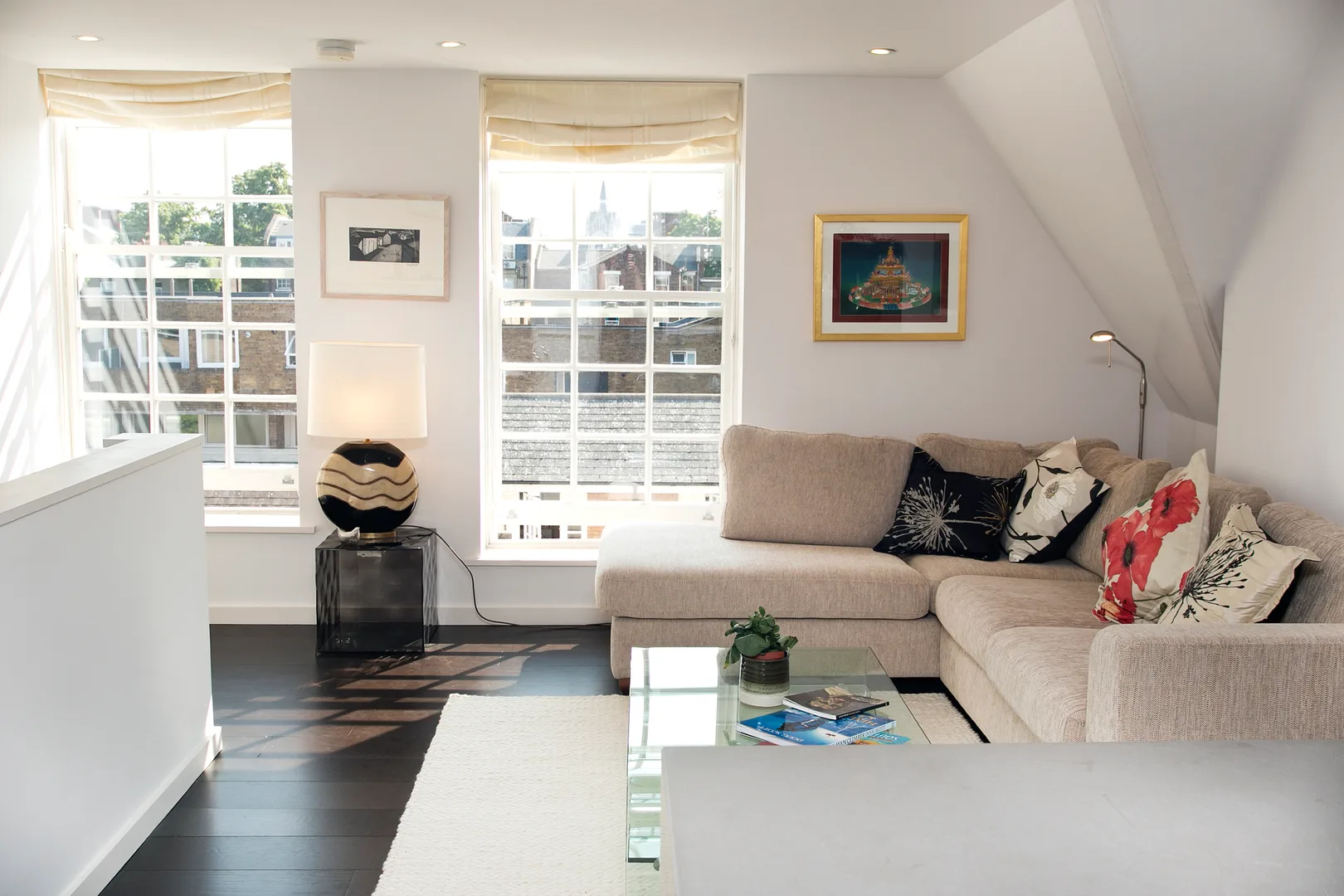 A bright living room with a sectional seating area, large windows, and a glass coffee table.
