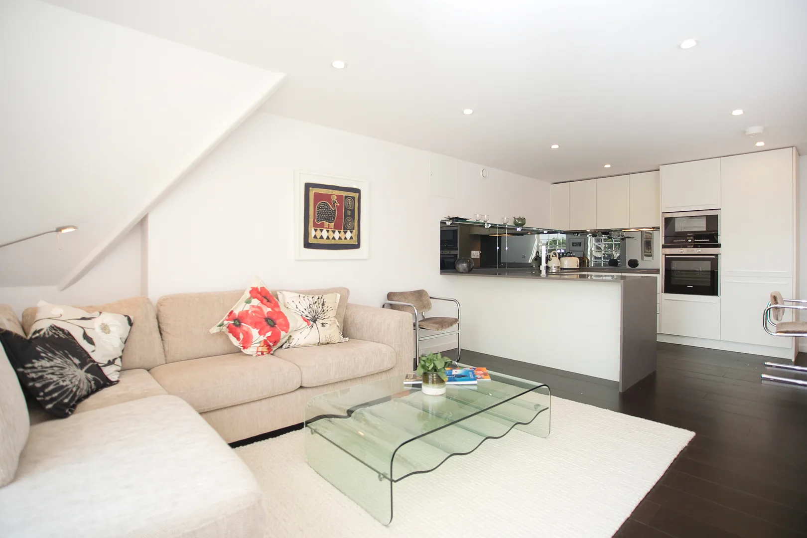 A bright open-plan living room and kitchen with a sectional sofa and glass coffee table.