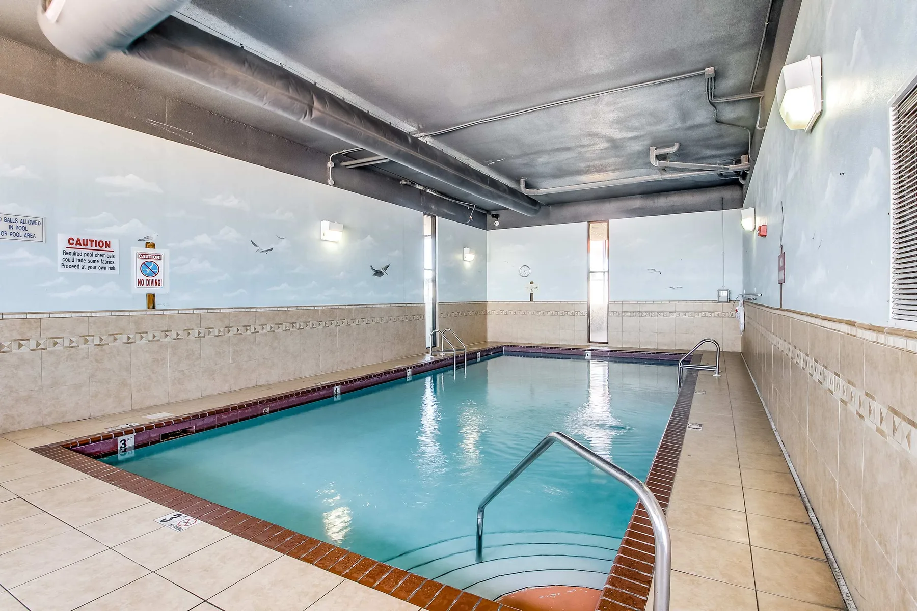 An indoor swimming pool with tiled walls and metal handrails.