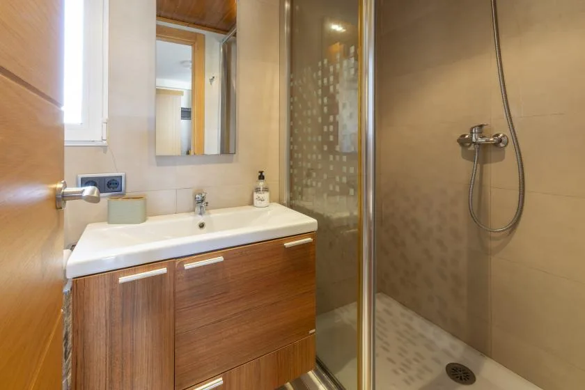 Un baño con mueble de lavabo de frente de madera, espejo y ducha de vidrio.
