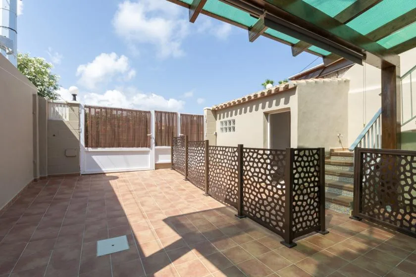 Un patio exterior embaldosado con paneles decorativos y una pérgola cubierta.