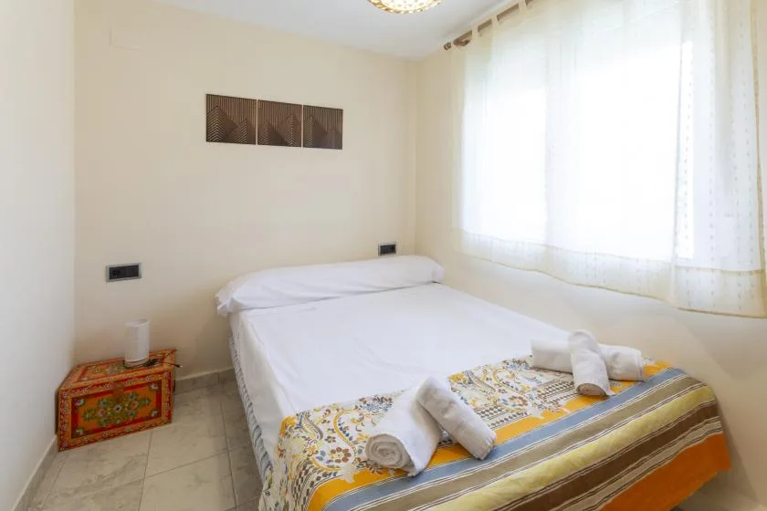 Un dormitorio con una cama bien tendida junto a una ventana luminosa.