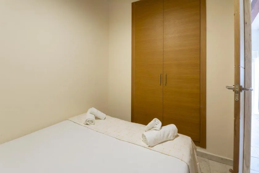 Un dormitorio con una cama tendida, toallas dobladas y un armario de madera.