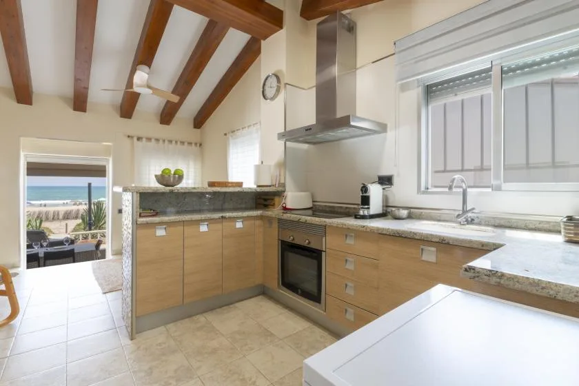 Una cocina luminosa con gabinetes de madera, una zona de cocción central y vigas expuestas en el techo.