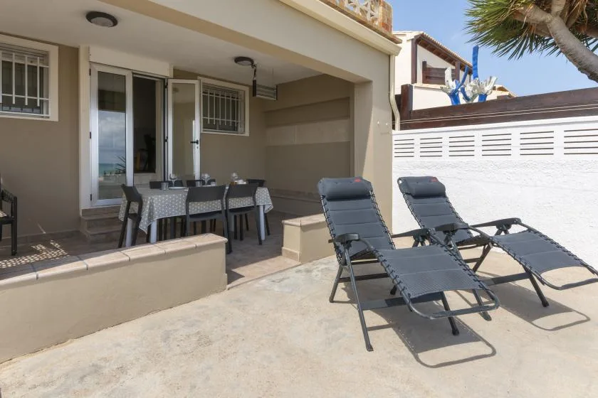 Un patio soleado tiene sillones reclinables junto a una zona de comedor cubierta.