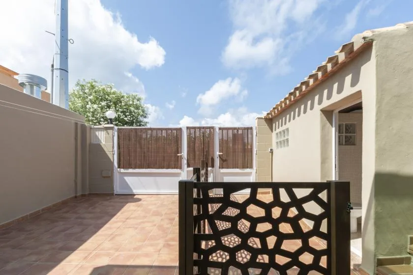 Un patio exterior con suelo de baldosas, una puerta calada y una entrada sombreada.