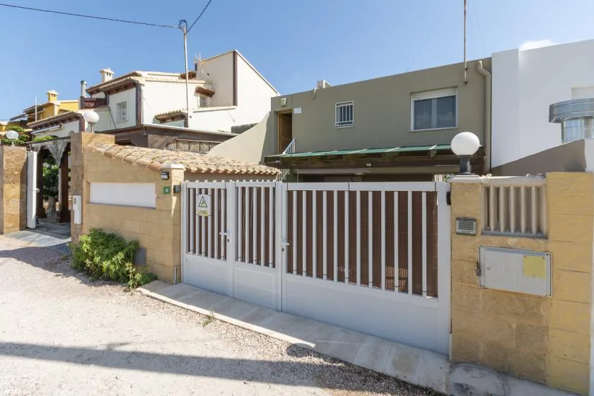 Un edificio moderno se alza detrás de una entrada con reja junto a una calle soleada.
