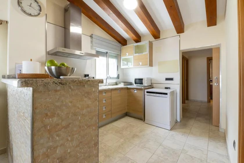 Una cocina luminosa con una encimera de aspecto pétreo, armarios de madera y vigas vistas.