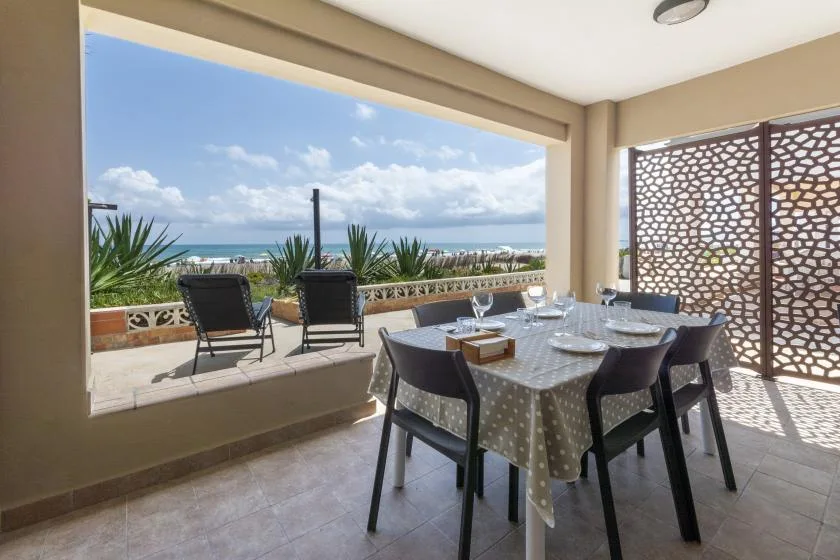 Comedor en una terraza cubierta con la mesa puesta y vistas al mar.
