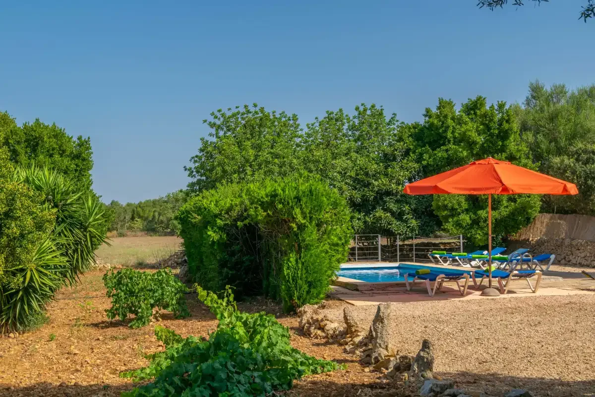 Una piscina al aire libre está junto a un patio de grava con una sombrilla naranja.