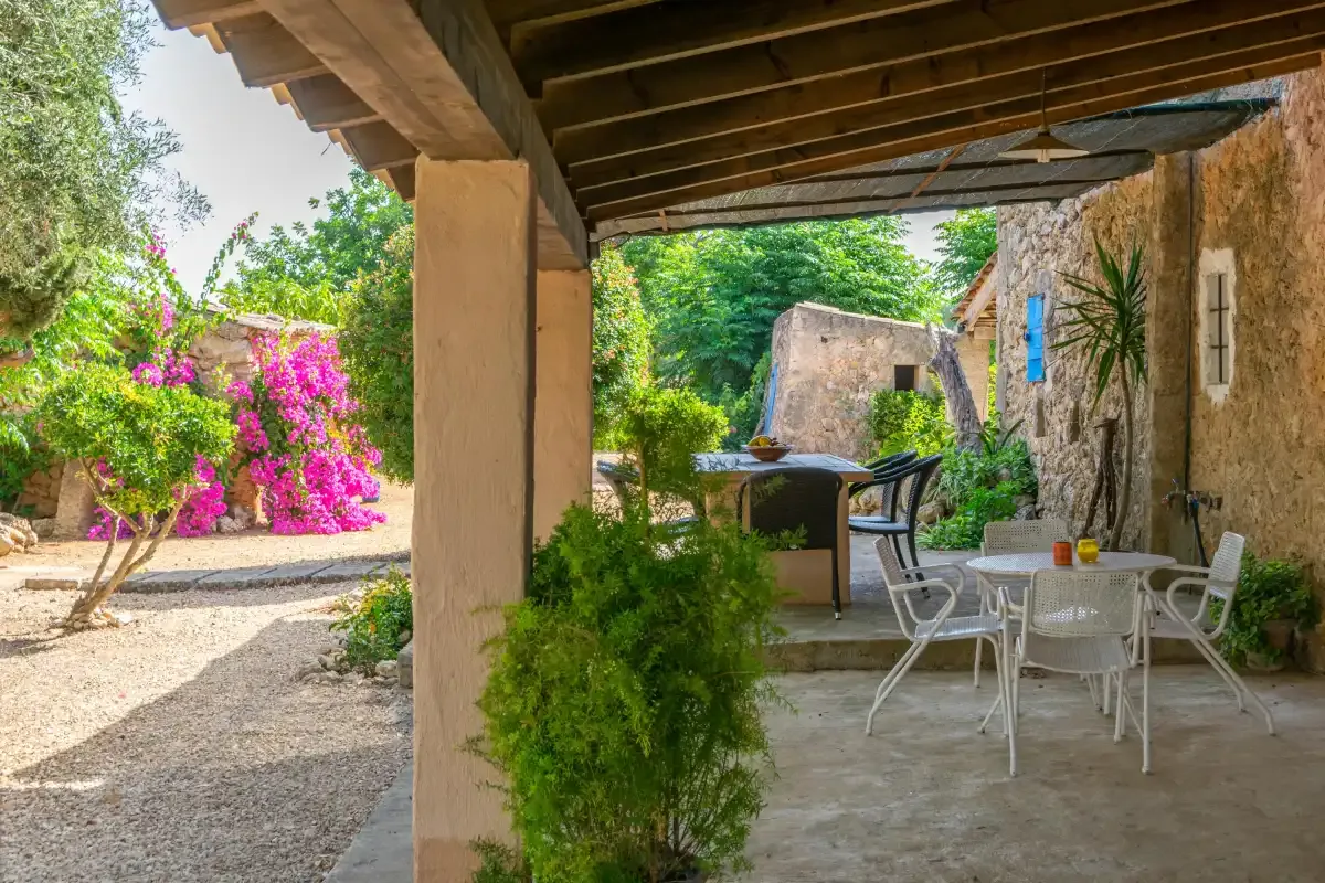 Un patio exterior cubierto con mesa y asientos junto a un jardín.
