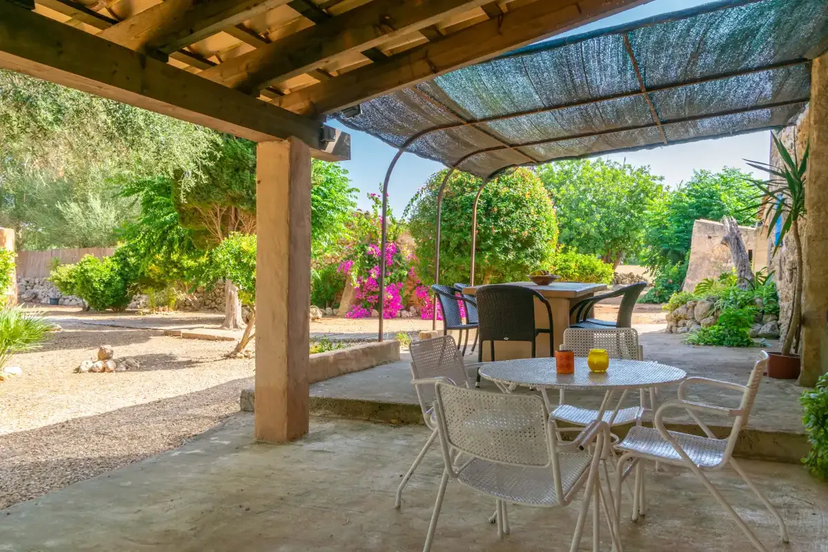 Un patio exterior sombreado con mesas y asientos da a un jardín frondoso.