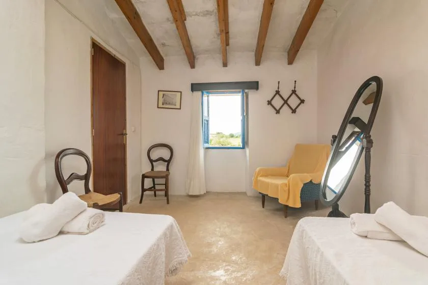 Un dormitorio luminoso con dos camas, una ventana y un sillón.