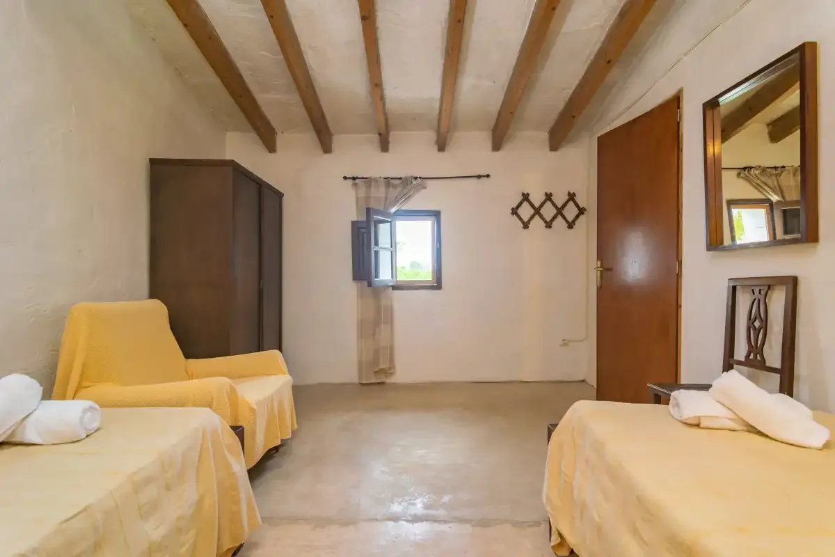 Un dormitorio con dos camas, un sillón amarillo y vigas expuestas en el techo.