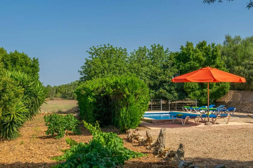 Una piscina al aire libre está junto a tumbonas bajo una sombrilla naranja.