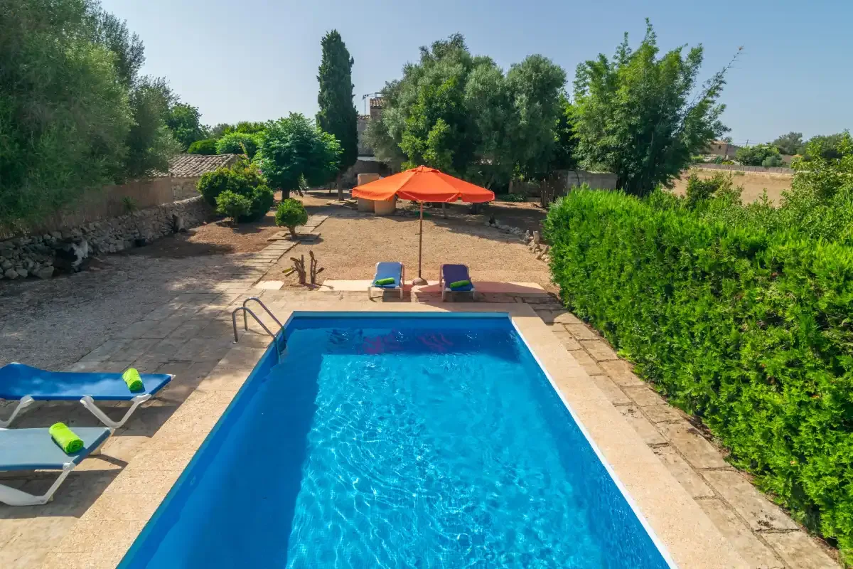 Una piscina exterior está junto a un patio pavimentado y una sombrilla naranja.
