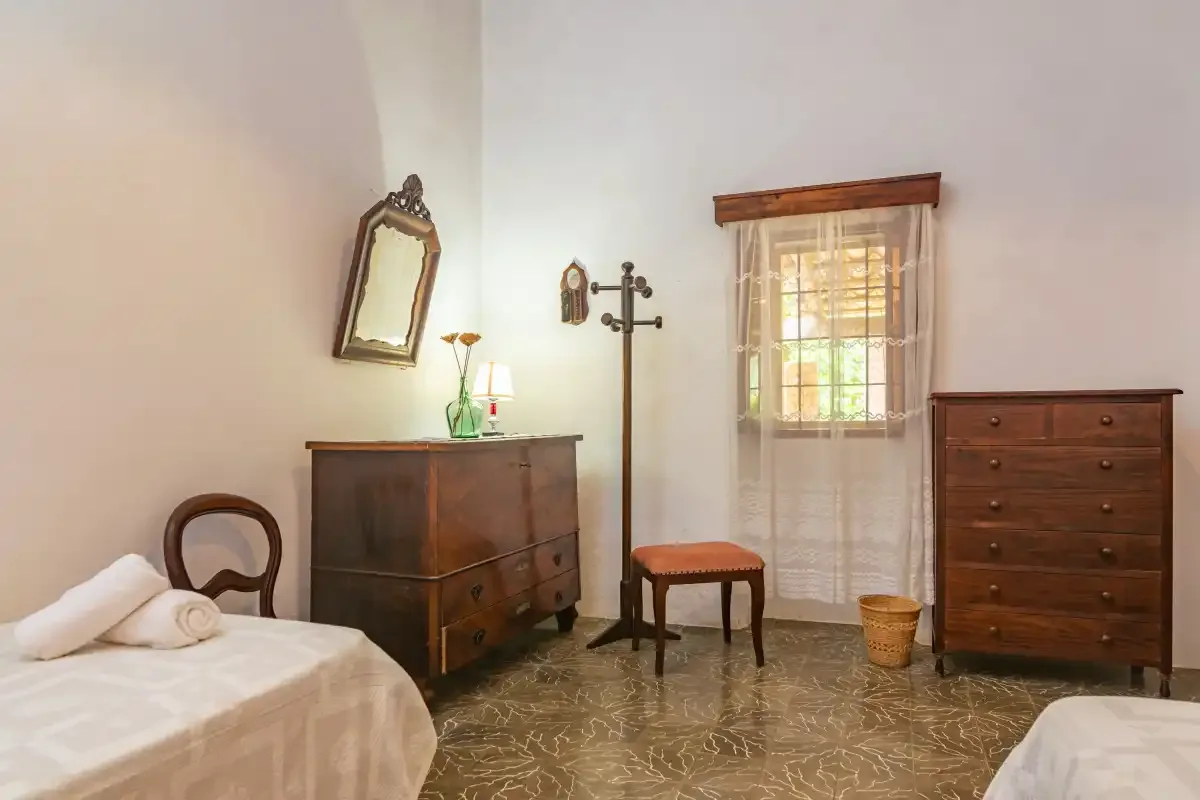 Un dormitorio con camas, cómodas de madera, una silla y una ventana.