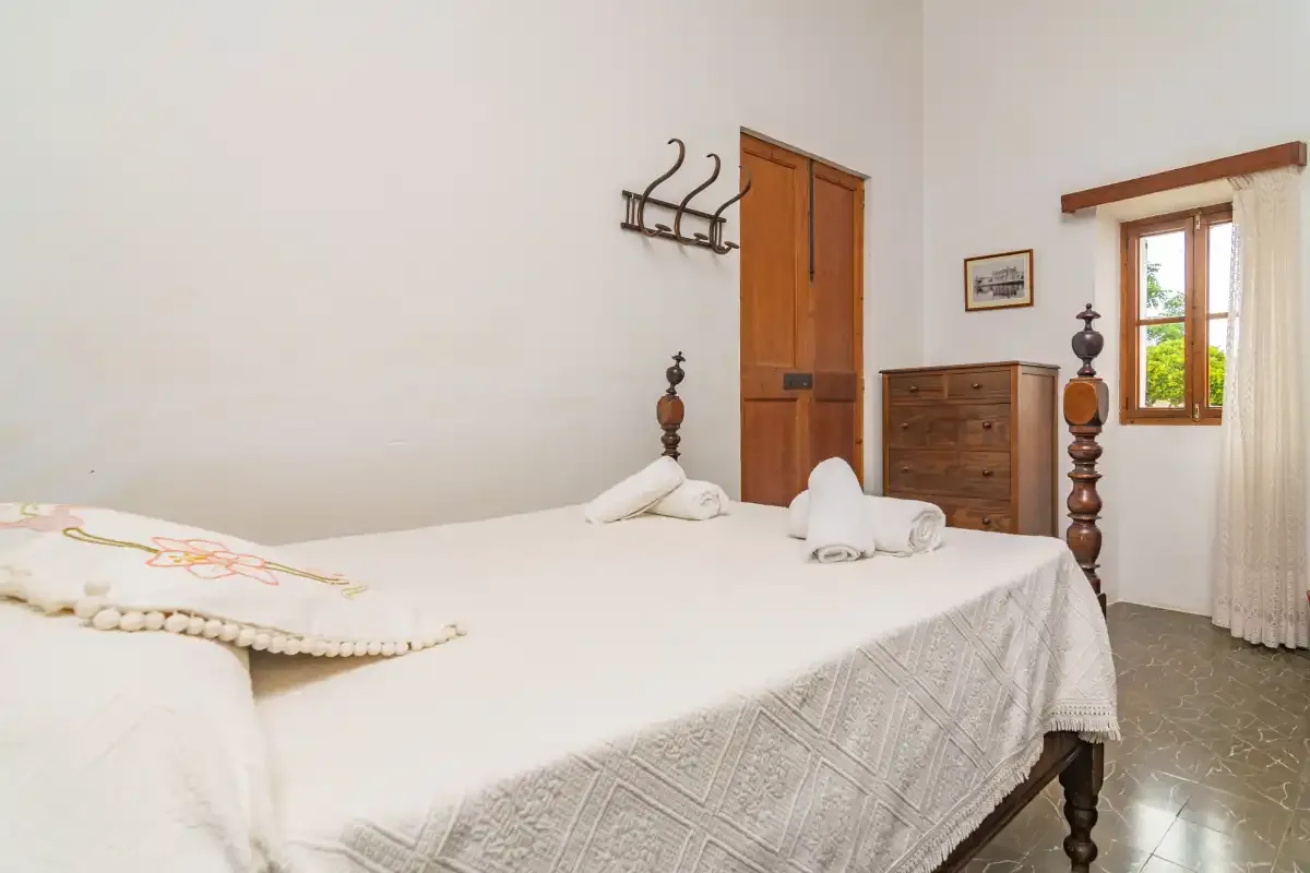 Un dormitorio con una cama bien tendida y una ventana de madera con vistas a la vegetación.