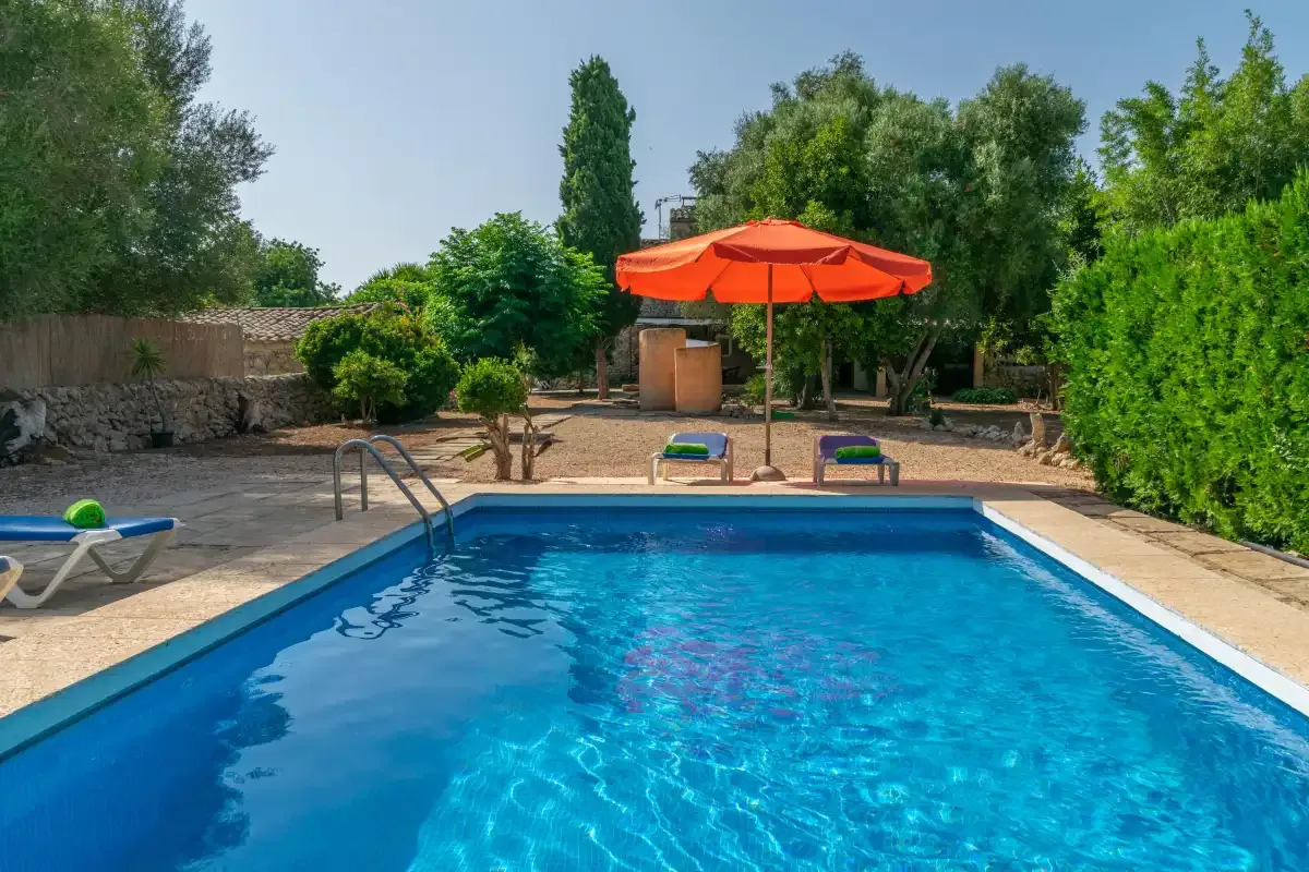 Una piscina al aire libre está junto a una sombrilla naranja y vegetación frondosa.