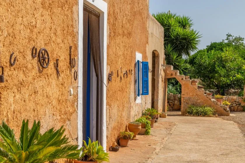Un edificio de estuco ocre da a un camino pavimentado con plantas en macetas.