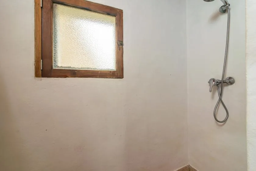 Un baño sencillo con una ducha de pared y una pequeña ventana translúcida.