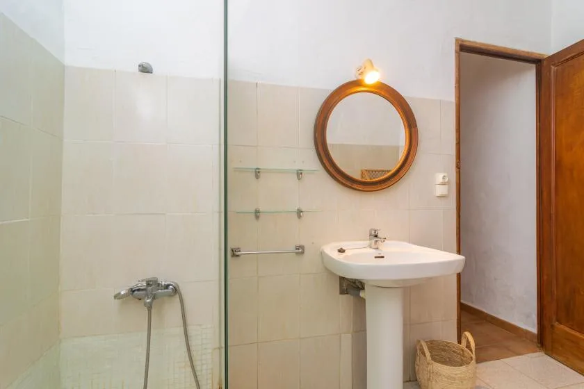 Un baño alicatado con lavabo de pared, espejo redondo y ducha.