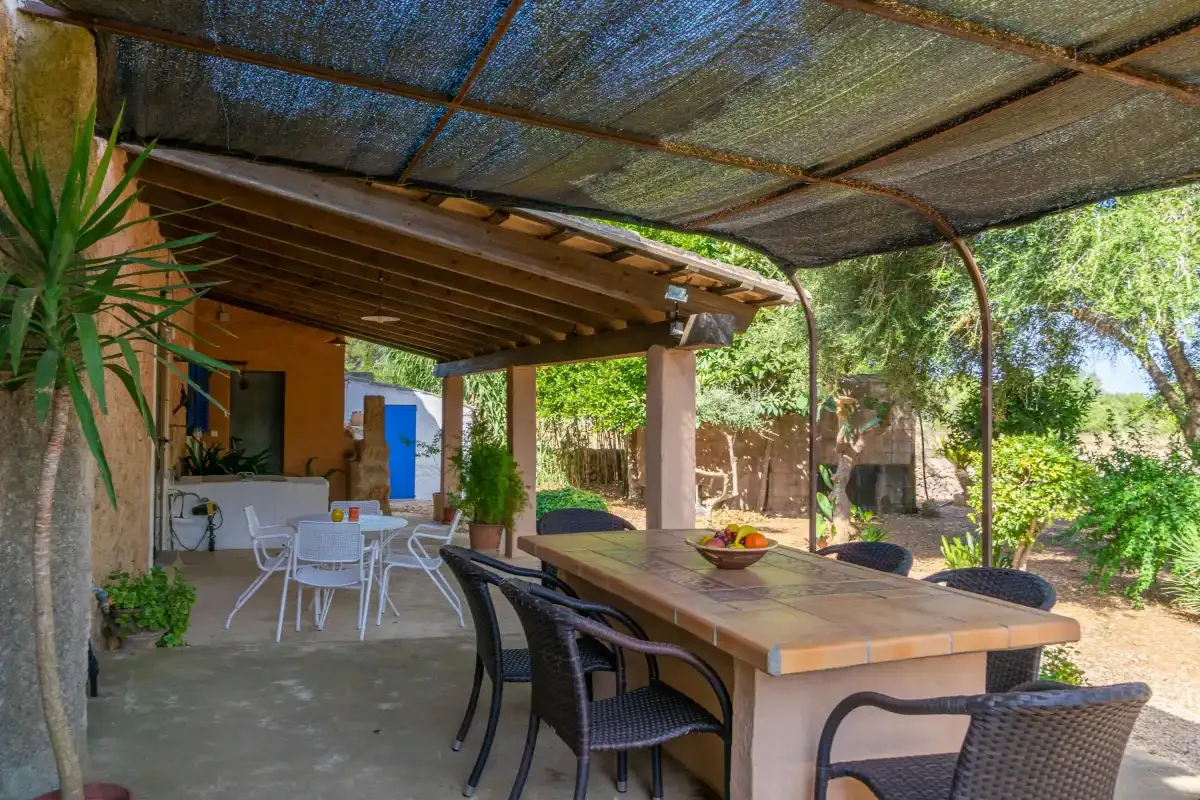 Un comedor exterior cubierto con una mesa larga y sillas junto a un patio abierto.