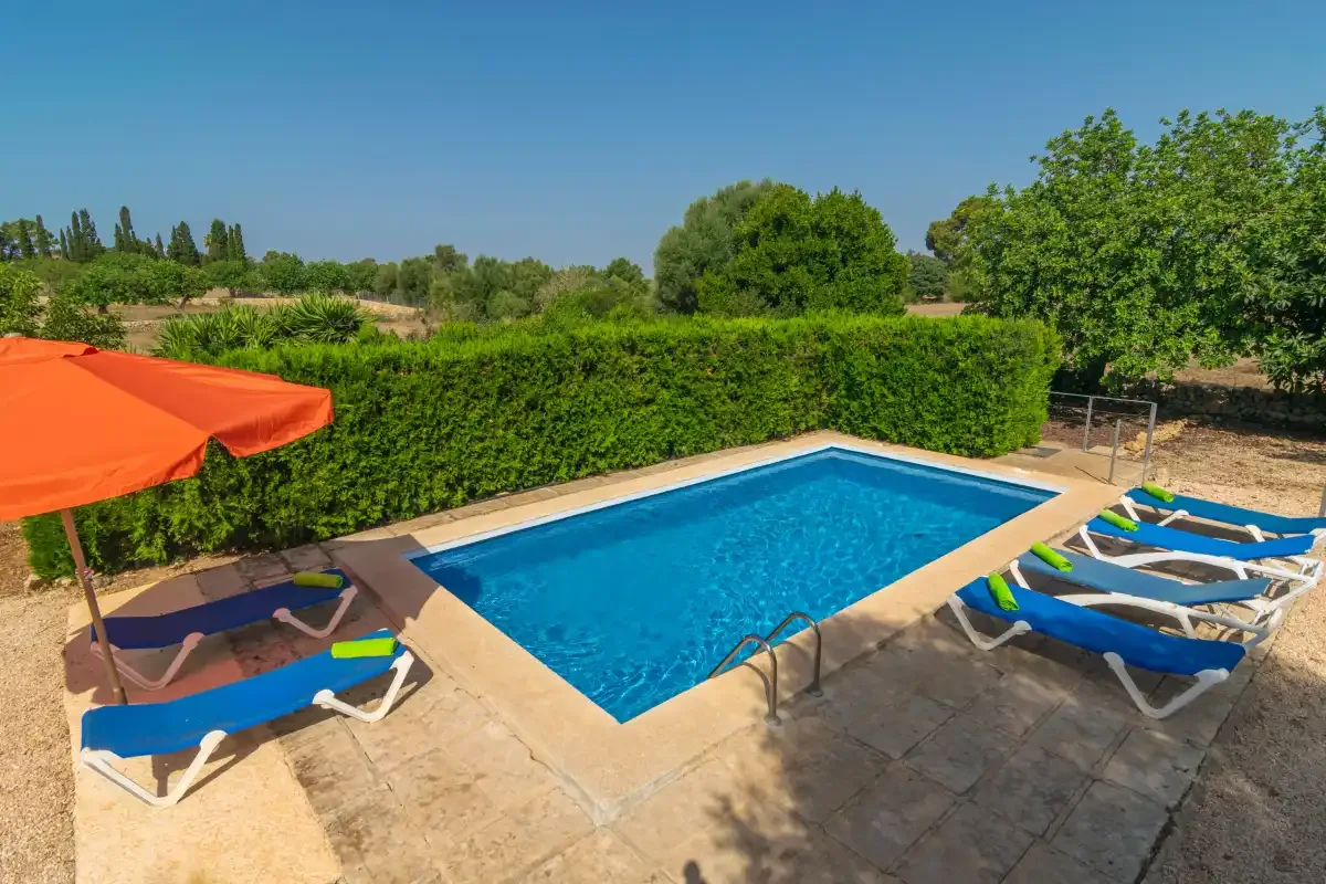 Una piscina al aire libre está rodeada de tumbonas y una sombrilla naranja.
