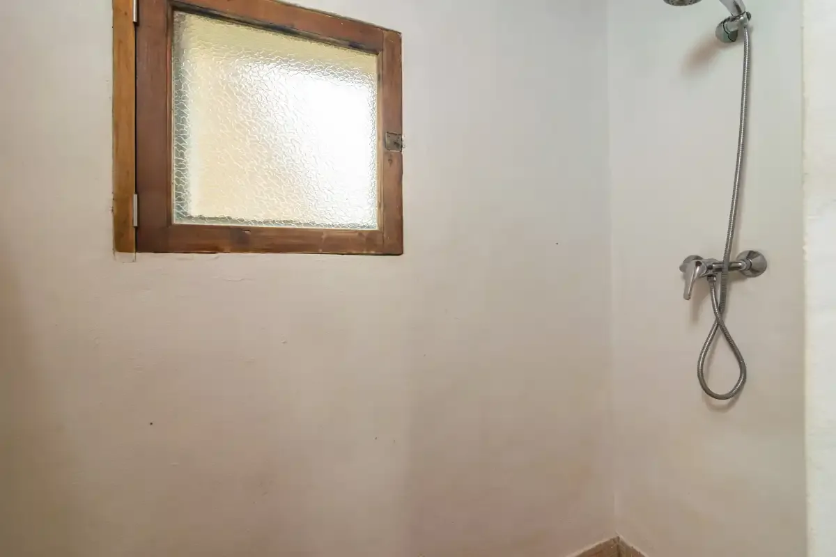 Una zona de ducha con un cabezal de pared y una pequeña ventana esmerilada.