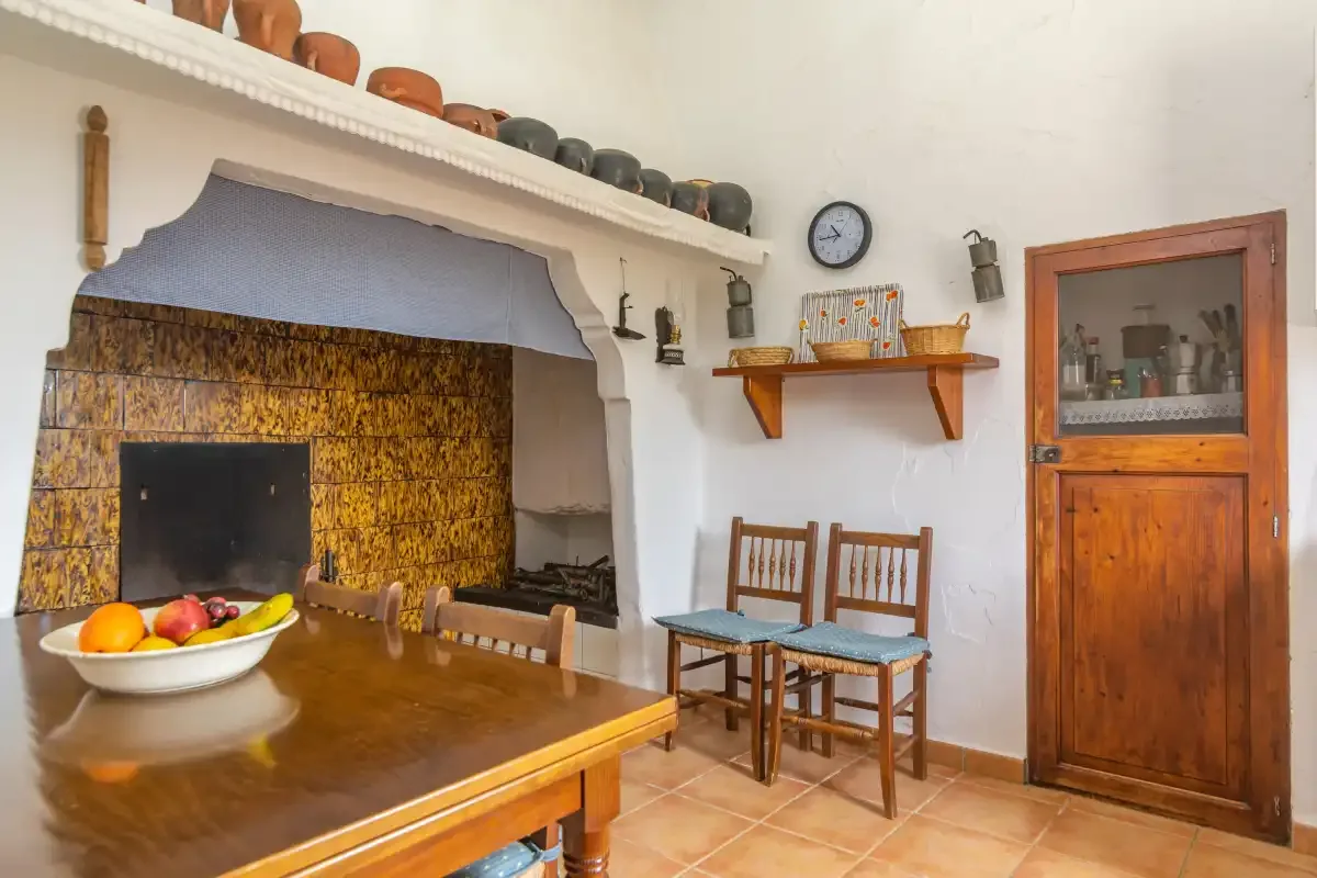 Un comedor rústico tiene una mesa de madera, sillas y una chimenea revestida de azulejos.