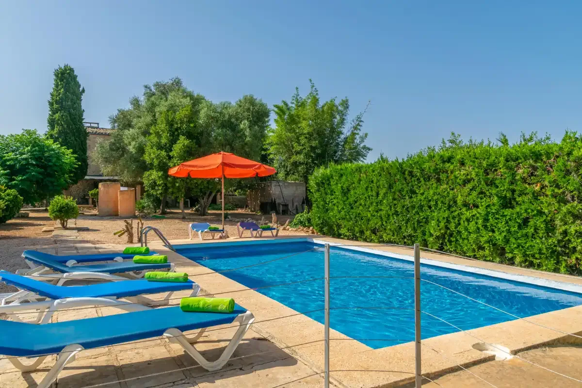 Una piscina al aire libre con asientos reclinables y una sombrilla roja.