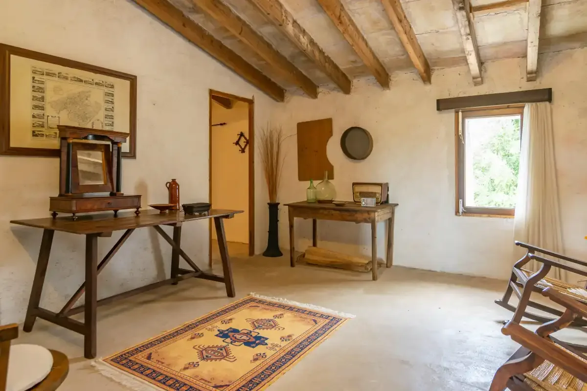 Una habitación rústica con vigas expuestas, mesas de madera y una alfombra estampada.