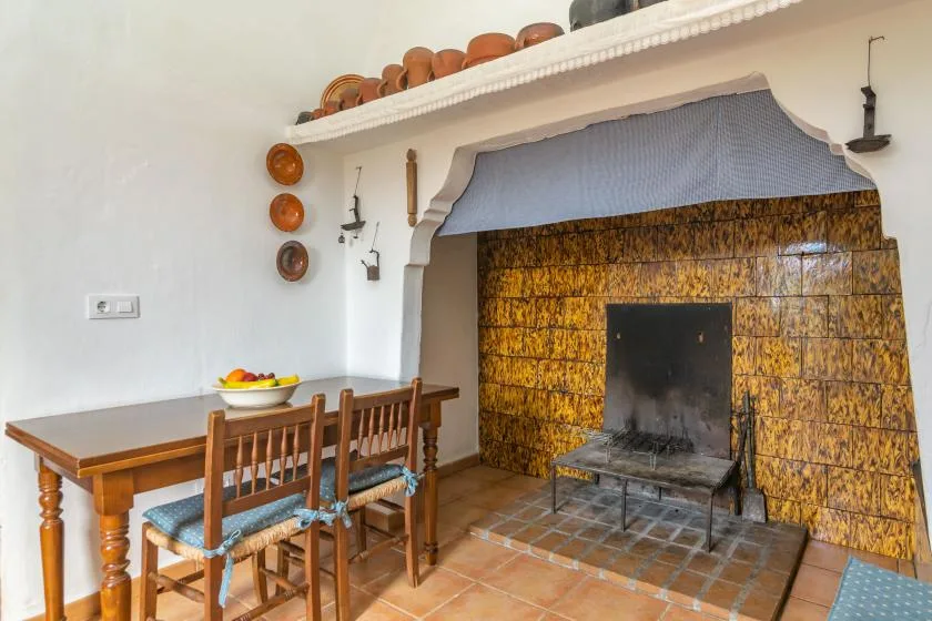 Un comedor junto a una gran chimenea revestida de azulejos, con mesa y sillas de madera.
