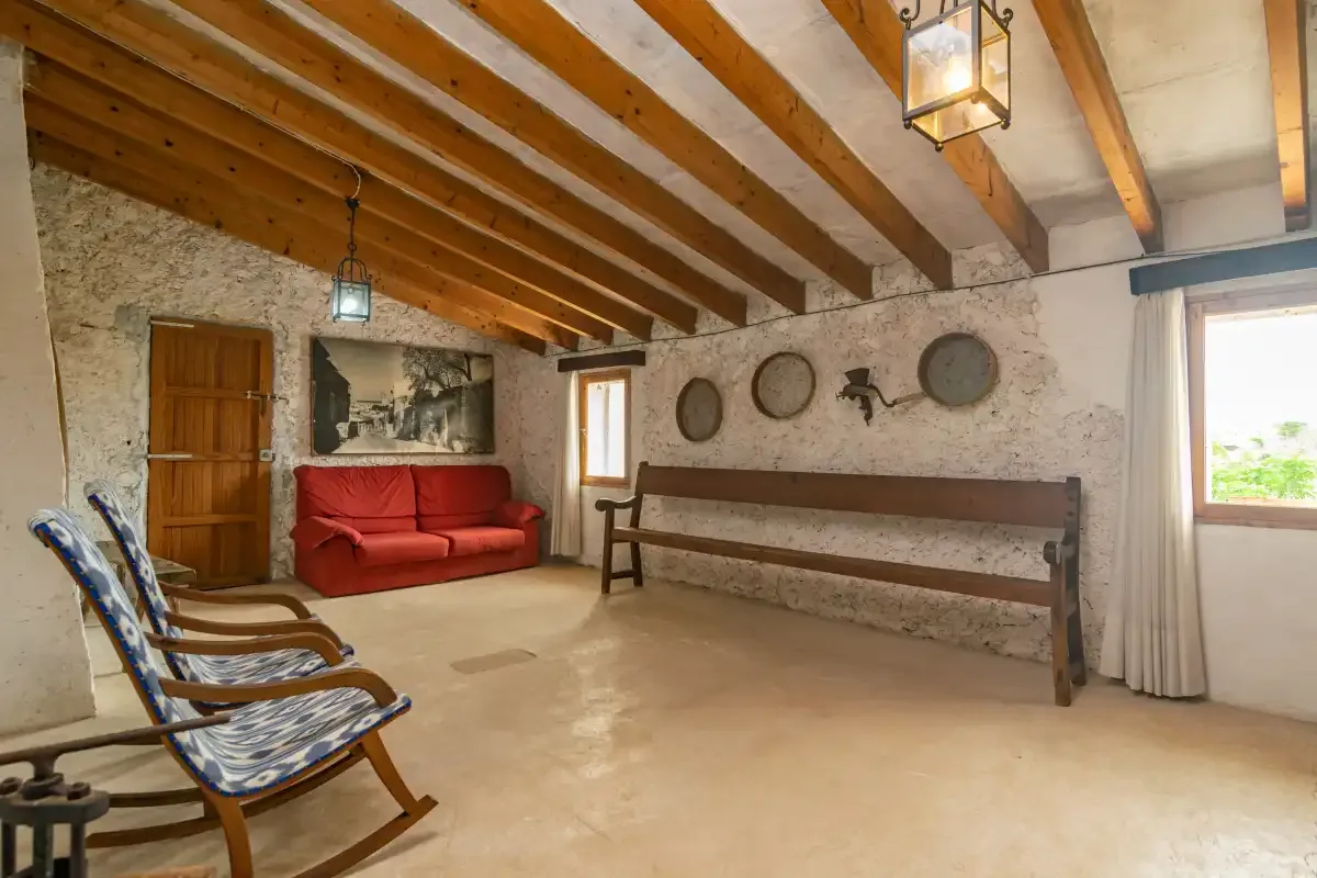 Una sala rústica con un sofá rojo, un banco de madera y vigas expuestas en el techo.