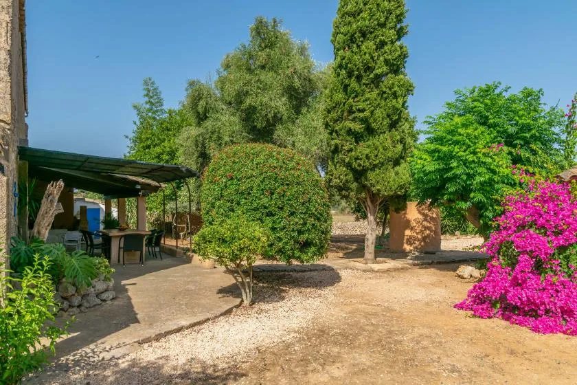 Un jardín con una zona de estar sombreada y arbustos con flores.