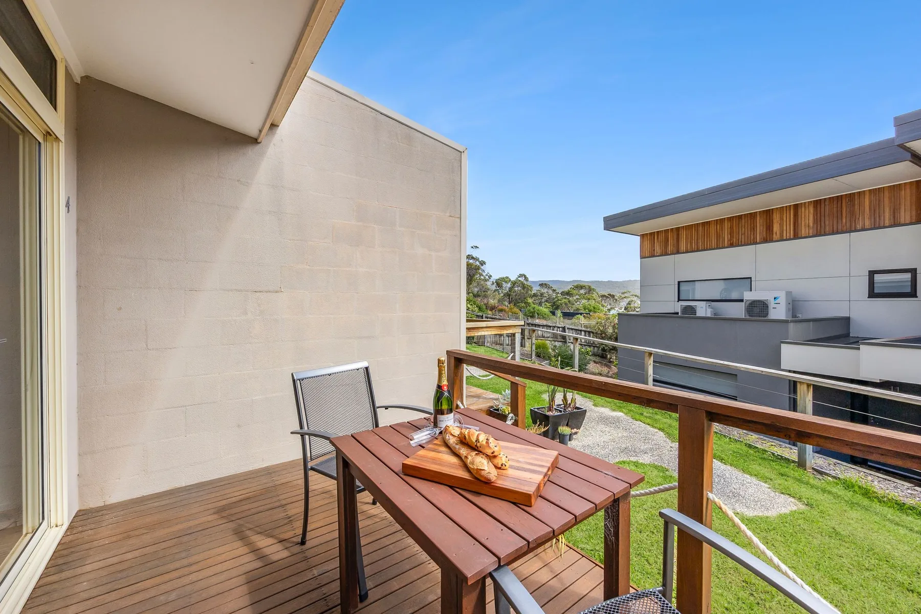 Outdoor dining area with a wooden table and chairs overlooking a grassy courtyard.