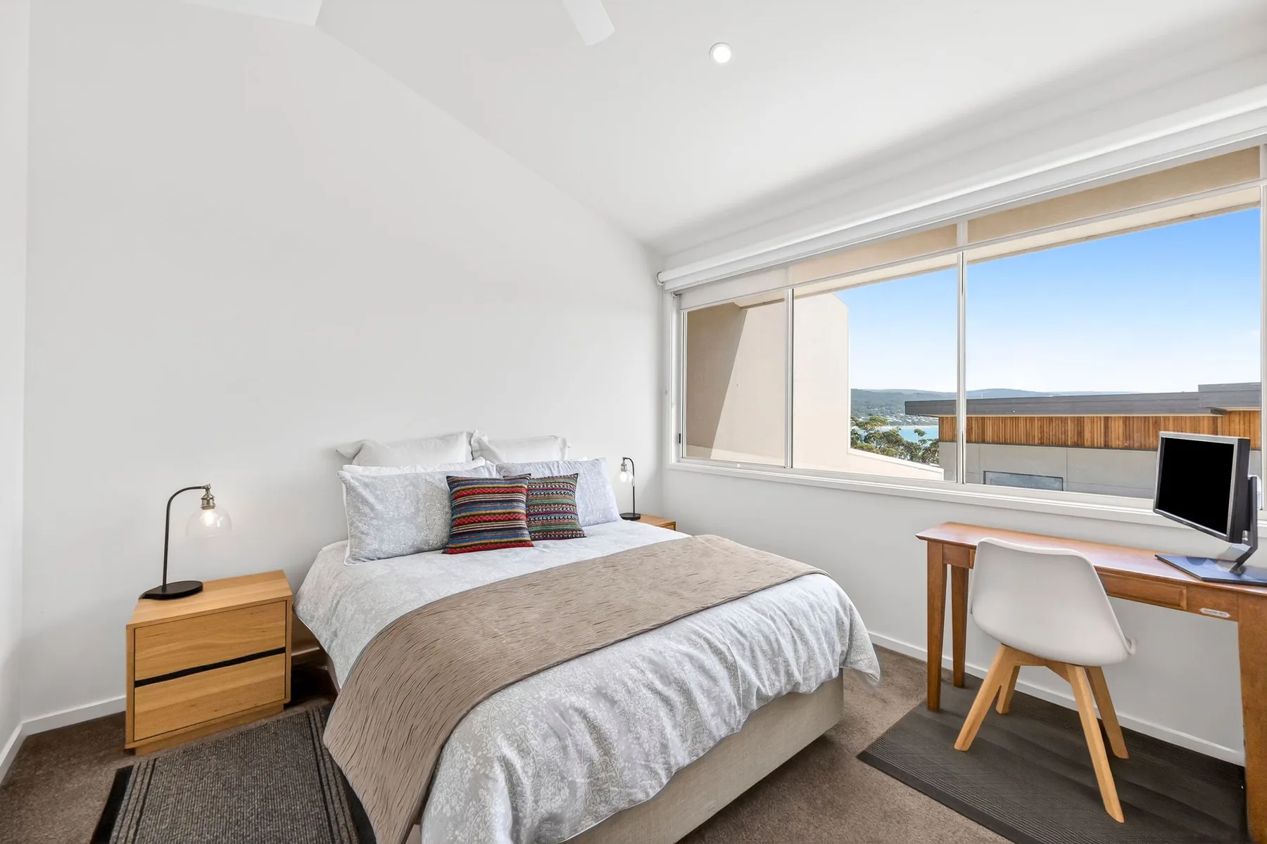 A bedroom with a bed beside a desk and large window.