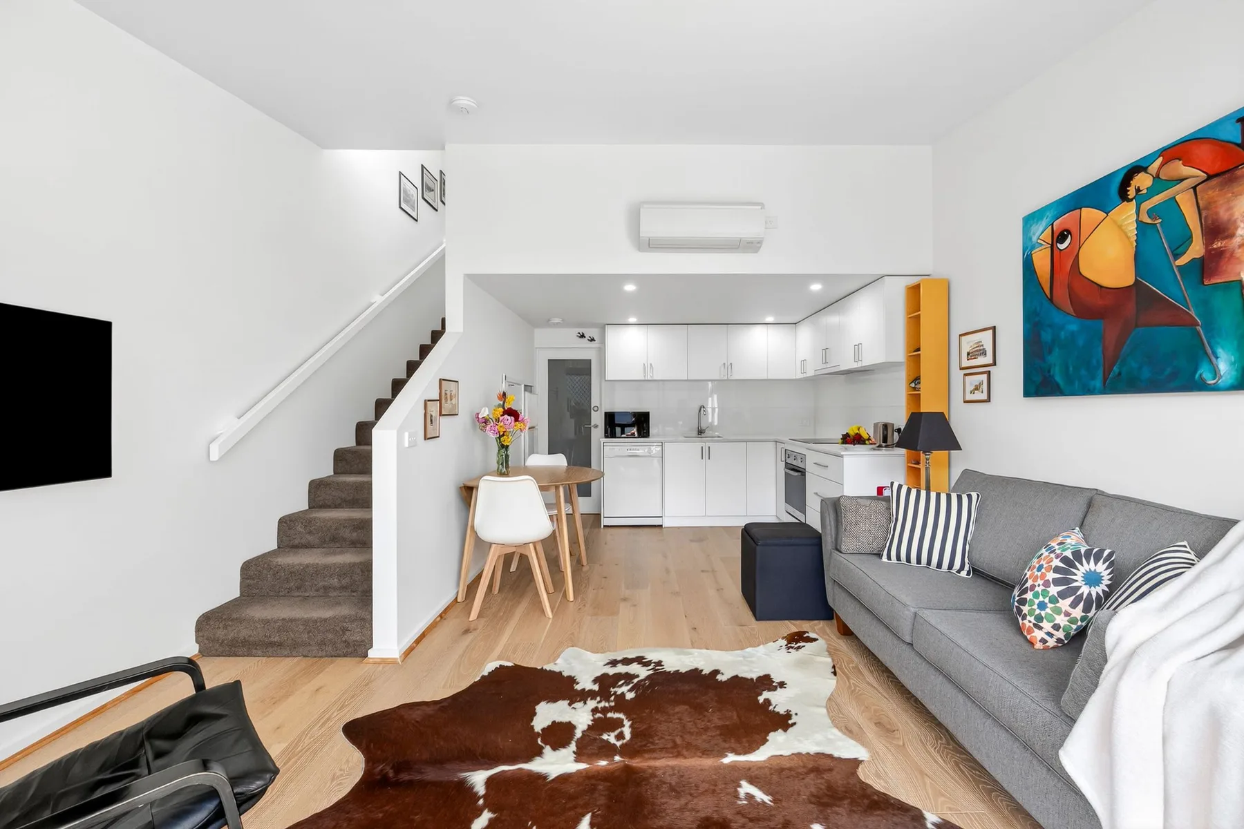 An open-plan living room with gray seating and a compact white kitchen.